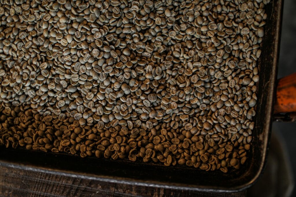 A large pile of unroasted coffee beans in a tray, perfect for coffee-related content.