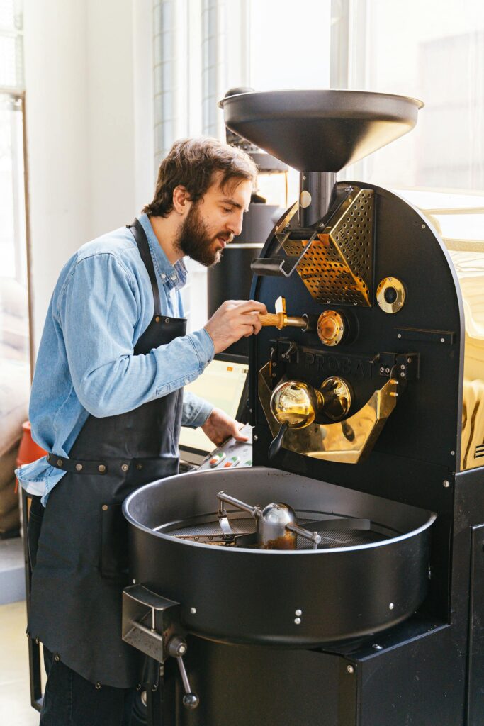Professional barista carefully working with industrial coffee roaster indoors.